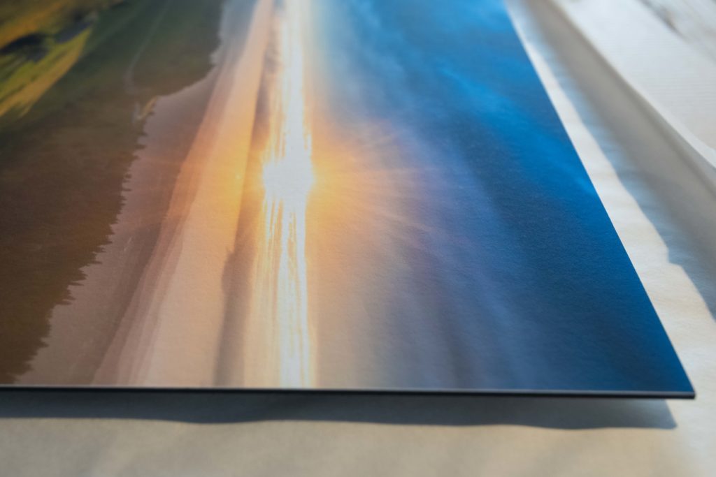DSC7910 Gros plan sur le bord d'un tirage photographique contrecollé sur une plaque rigide : un coucher de soleil sur l'eau, la tranche du support bien visible